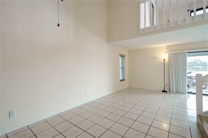 Loft-style living space featuring neutral tile flooring, high ceilings, large sliding glass doors, and an upper-level balcony with white railings