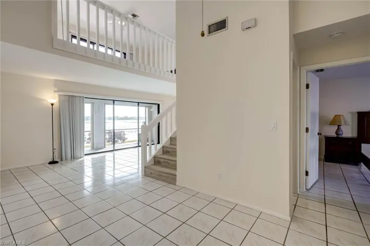 Living space with large format tile flooring, a staircase with white wood railing, and a second-story interior balcony