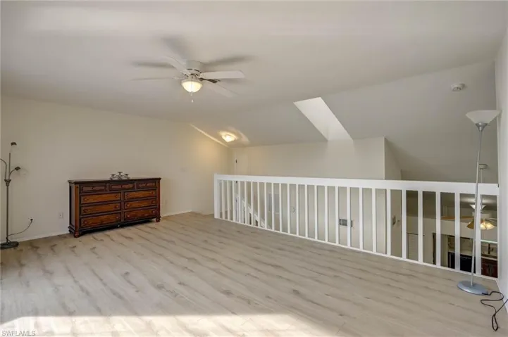 Bright open loft with wood-finish flooring, white railing, sloped ceiling, and ceiling fan