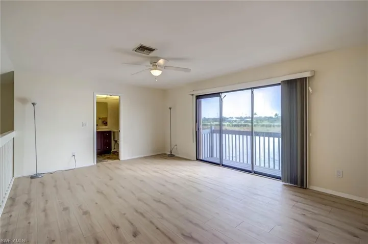 Light wood-finish flooring, ceiling fan with integrated lighting, sliding glass doors, private balcony with water frontage, interior half-wall with railing