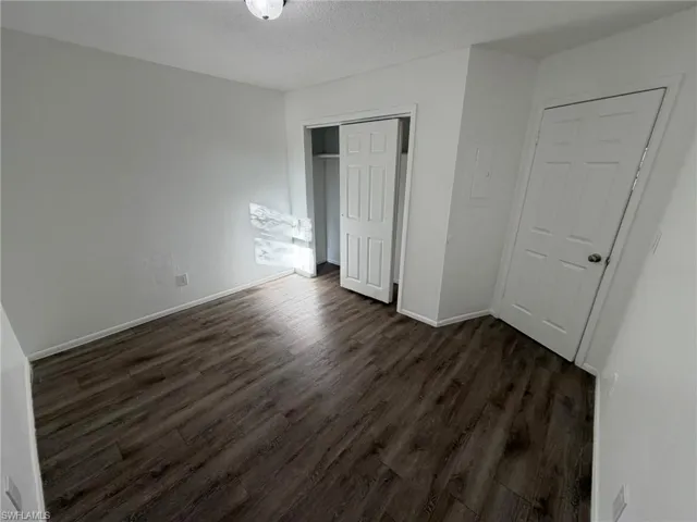 Unfurnished bedroom with a textured ceiling, a closet, and dark wood-style floors
