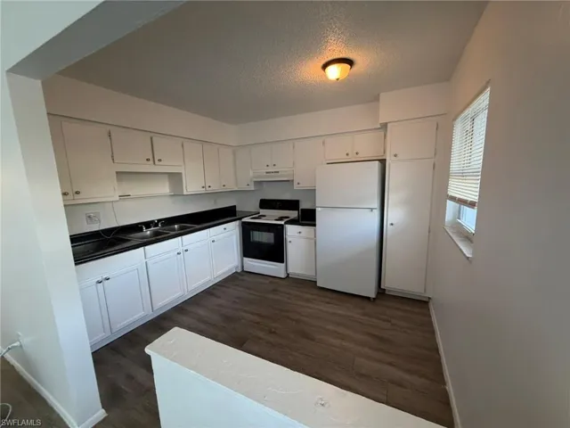 Kitchen featuring white cabinets, white appliances, a textured ceiling, dark wood-style floors, and dark countertops