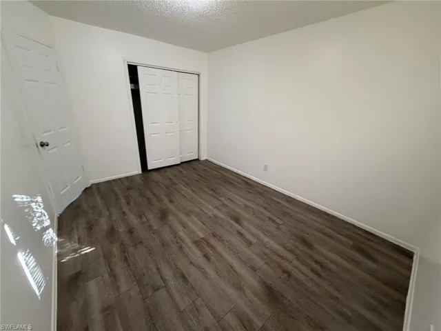 Unfurnished bedroom with a textured ceiling, dark wood-style floors, and a closet