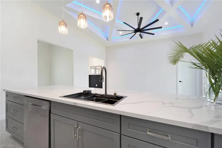 Kitchen featuring gray cabinets, coffered ceiling, light stone counters, stainless steel dishwasher, and a ceiling fan