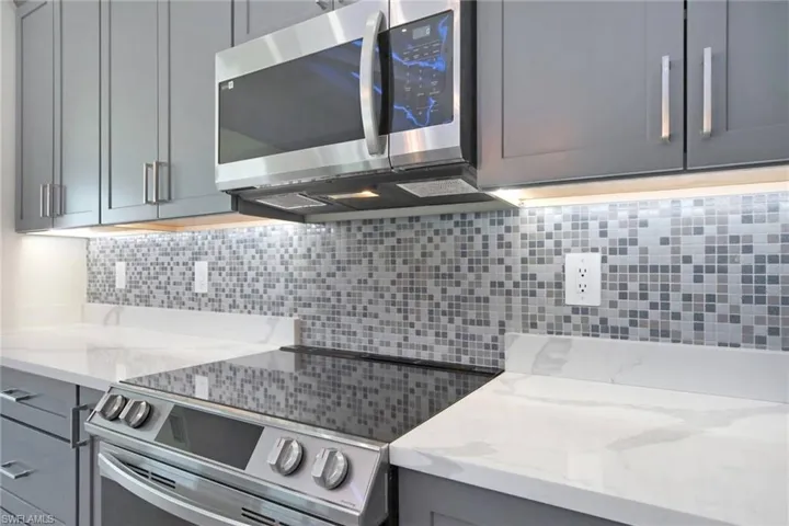 Kitchen with decorative backsplash, appliances with stainless steel finishes, gray cabinets, and light stone countertops