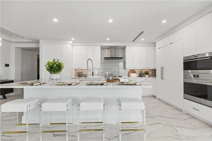 Kitchen featuring white cabinets, wall chimney range hood, decorative backsplash, a center island with sink, and a breakfast bar
