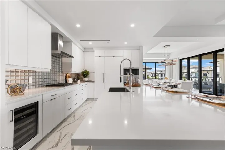 Kitchen with wine cooler, wall chimney exhaust hood, stainless steel gas stovetop, tasteful backsplash, and white cabinetry