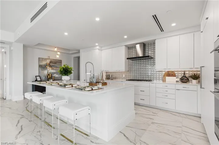 Kitchen with an island with sink, a kitchen breakfast bar, wall chimney exhaust hood, and white cabinetry