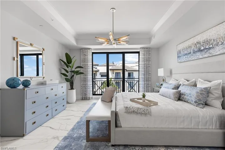 Bedroom featuring a raised ceiling, ceiling fan with notable chandelier, and access to outside