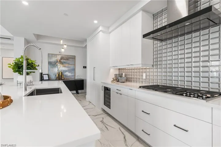 Kitchen with wall chimney exhaust hood, stainless steel gas cooktop, sink, decorative backsplash, and white cabinets