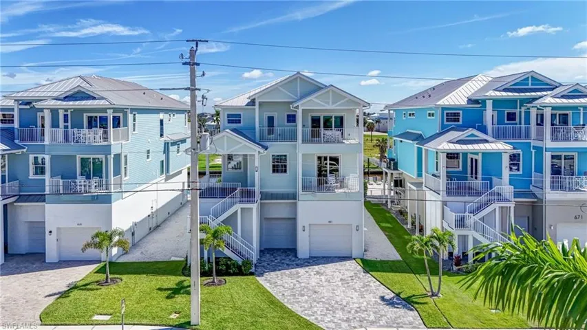 Coastal home featuring a residential view, an attached garage, decorative driveway, a front lawn, and a balcony - Virtually Edited Image