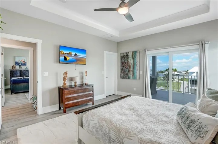 Bedroom featuring a tray ceiling, access to exterior, light wood-style floors, and ceiling fan - Virtually Edited Image