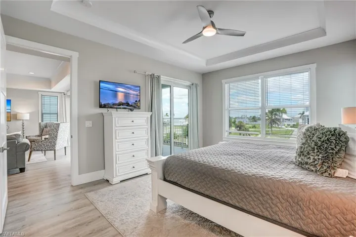Bedroom featuring a raised ceiling, access to outside, light wood-type flooring, and a ceiling fan - Virtually Edited Image