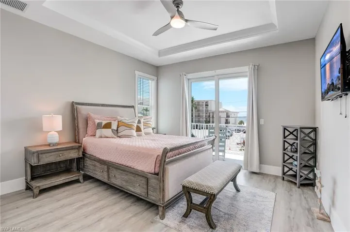Bedroom with a raised ceiling, light wood finished floors, access to exterior, and a ceiling fan - Virtually Edited Image