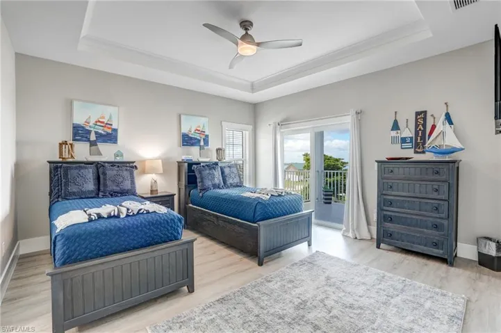 Bedroom with a raised ceiling, light wood-style floors, and access to outside - Virtually Edited Image