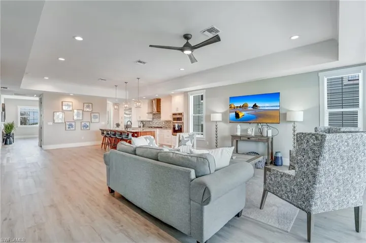 Great Room with a tray ceiling, a ceiling fan, light wood finished floors, and recessed lighting - Virtually Edited Image