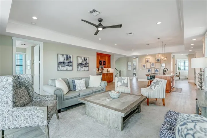 Great room with light wood-style flooring, ceiling fan, a raised ceiling, recessed lighting, and a chandelier - Virtually Edited Image