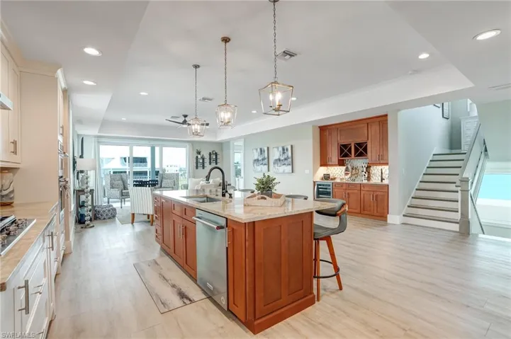 Kitchen with brown cabinets, a breakfast bar, hanging light fixtures, a kitchen island with sink, and light wood-style floors - Virtually Edited Image