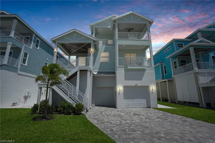 Coastal inspired home featuring stucco siding, a front lawn, decorative driveway, a garage, and stairway - Virtually Edited Image