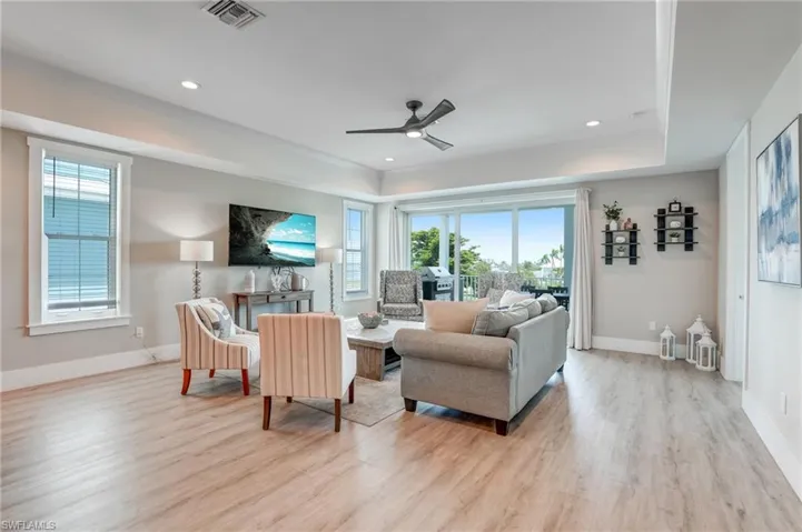 Great Room featuring ceiling fan, light wood finished floors, a tray ceiling, and recessed lighting - Virtually Edited Image