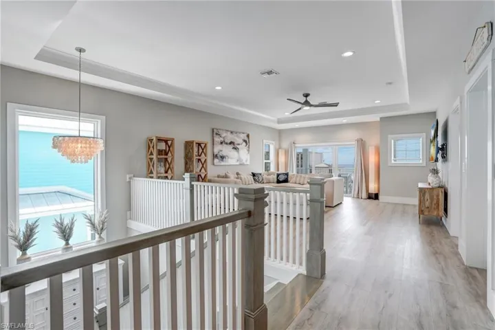 Upstairs Entryway to Grand Living Room with a tray ceiling, light wood-style flooring, recessed lighting, and an upstairs landing - Virtually Edited Image