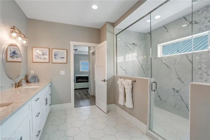 Full bath featuring a marble finish shower, a ceiling fan, double vanity, and light tile patterned floors - Virtually Edited Image