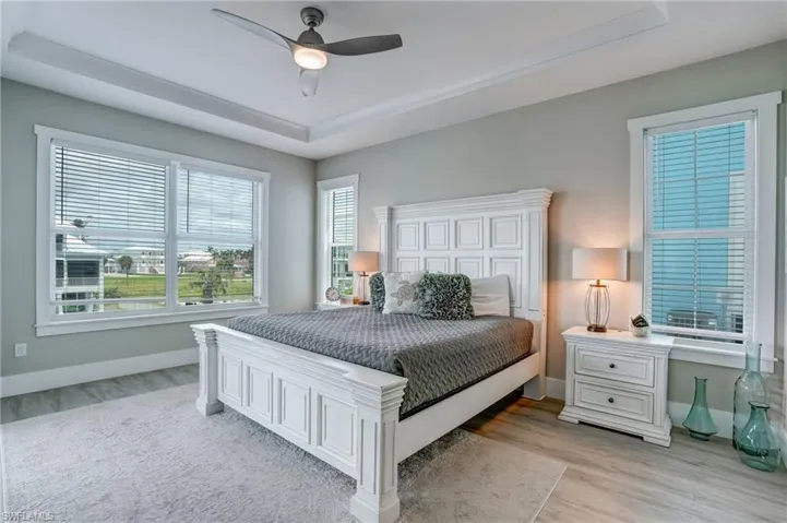 Bedroom with a raised ceiling, light wood-style floors, and a ceiling fan - Virtually Edited Image