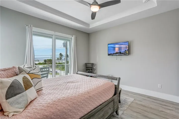 Bedroom with a raised ceiling, access to exterior, wood finished floors, and ceiling fan - Virtually Edited Image
