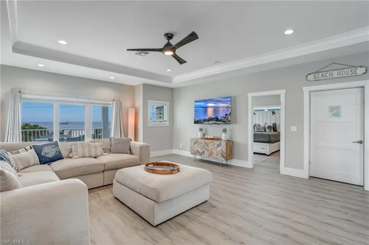 Grand Living area with light wood-style flooring, a raised ceiling, a ceiling fan, and recessed lighting - Virtually Edited Image