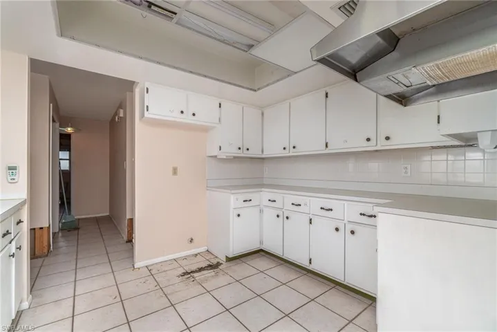 Kitchen featuring light tile patterned flooring, wall chimney range hood, tasteful backsplash, and white cabinetry