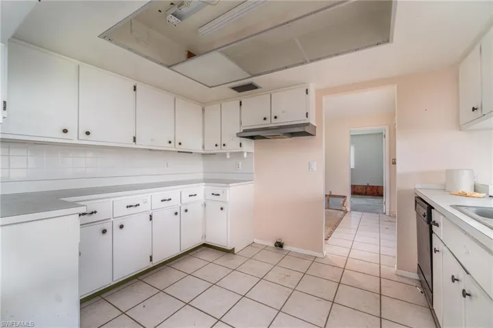 Kitchen with decorative backsplash, sink, black dishwasher, white cabinetry, and light tile patterned flooring