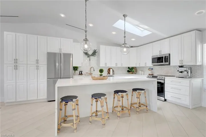 Kitchen featuring a skylight, stainless steel appliances, white cabinetry, hanging light fixtures, and lofted ceiling
