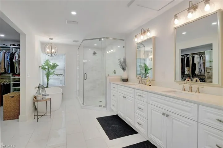 Bathroom featuring a walk in closet, double vanity, a shower stall, a freestanding bath, and a chandelier