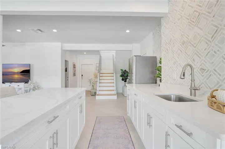 Kitchen featuring light stone counters, freestanding refrigerator, white cabinetry, and recessed lighting