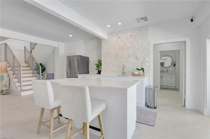 Kitchen with white cabinets, freestanding refrigerator, a breakfast bar area, beam ceiling, and light stone counters