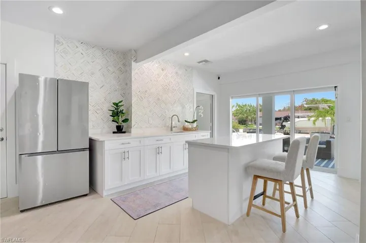 Kitchen with freestanding refrigerator, white cabinets, a breakfast bar, a kitchen island, and light stone counters