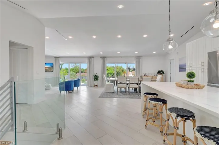 Kitchen with a breakfast bar area, white cabinetry, light wood-type flooring, light stone counters, and stainless steel refrigerator