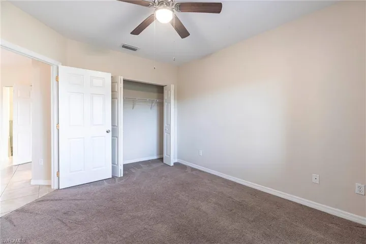 Unfurnished bedroom featuring light colored carpet, baseboards, a closet, and ceiling fan