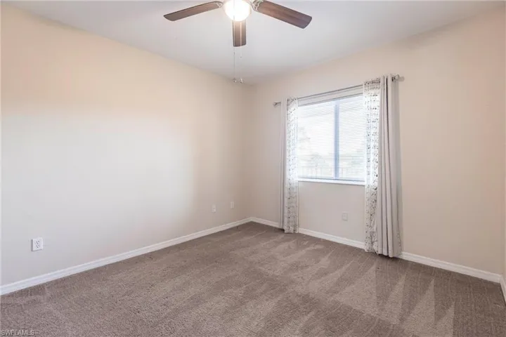 Carpeted empty room with ceiling fan and baseboards