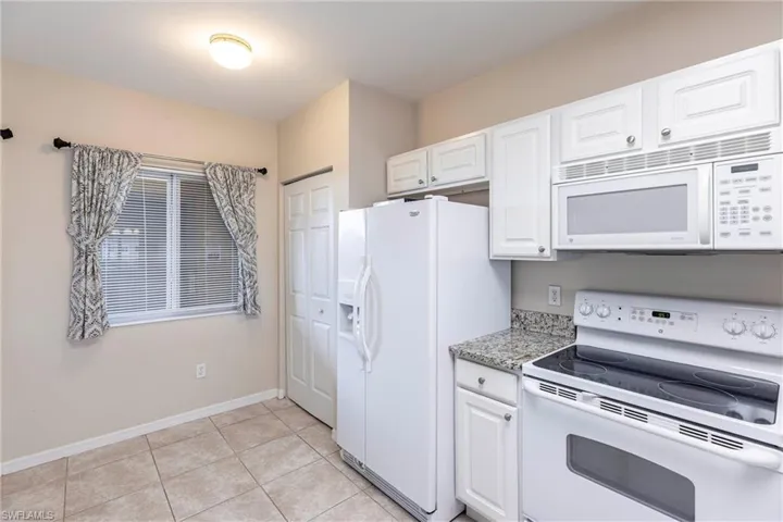 Kitchen with white appliances, white cabinetry, light tile patterned floors, and light stone countertops