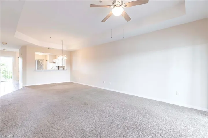 Unfurnished room with a tray ceiling, carpet flooring, baseboards, a chandelier, and a ceiling fan
