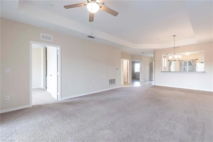 Unfurnished living room with a raised ceiling, carpet flooring, baseboards, ceiling fan, and a chandelier