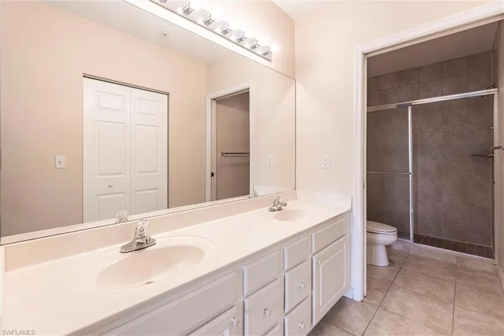 Full bath featuring toilet, double vanity, tile patterned flooring, and a shower stall