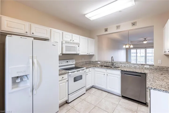 Kitchen featuring white appliances, a sink, white cabinets, light tile patterned floors, and light stone countertops