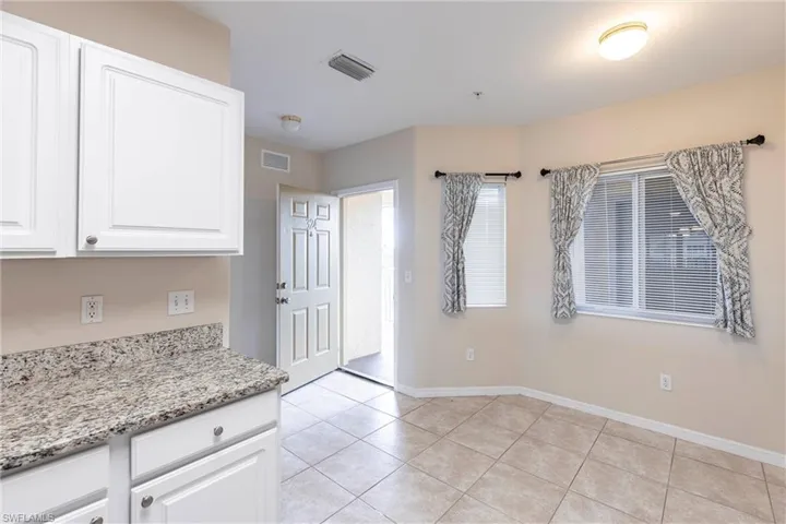 Kitchen with light tile patterned flooring, white cabinets, baseboards, and light stone countertops