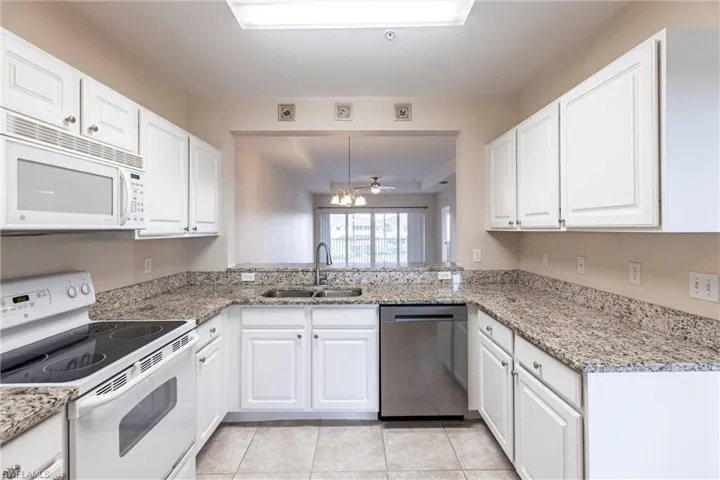 Kitchen featuring white appliances, a sink, white cabinets, light tile patterned floors, and light stone countertops