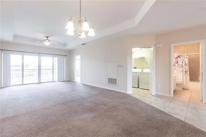 Unfurnished room featuring washer and clothes dryer, a raised ceiling, a chandelier, a ceiling fan, and light carpet