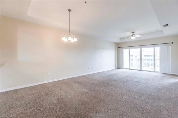 Carpeted empty room with a raised ceiling, baseboards, ceiling fan, and a chandelier