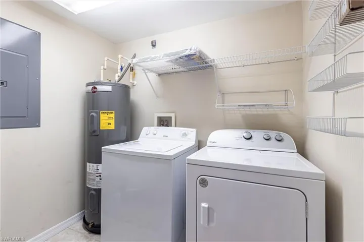 Laundry room featuring electric panel, washing machine and dryer, electric water heater, baseboards, and tile patterned flooring
