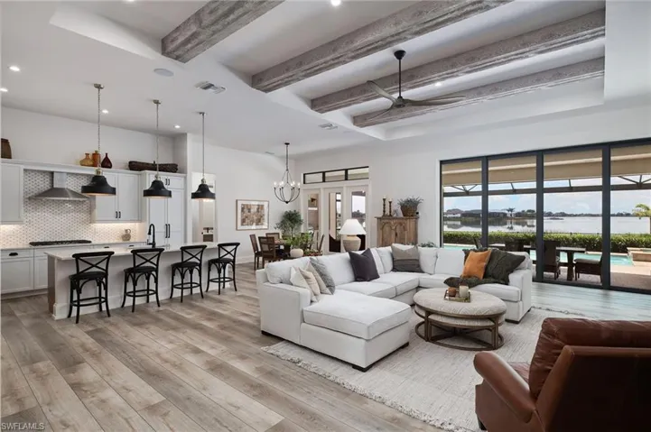 Living room with sink, light hardwood / wood-style flooring, ceiling fan with notable chandelier, and beamed ceiling